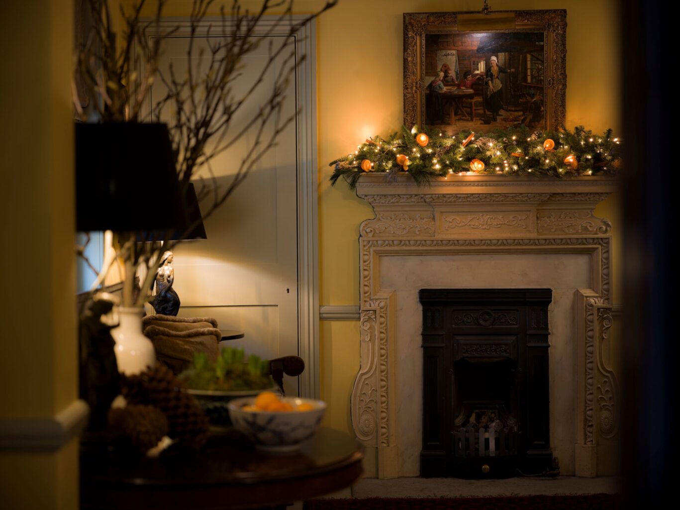 Ornate fireplace at The Rookery decorated with a festive garland of evergreens and warm lights beneath a large framed painting.
