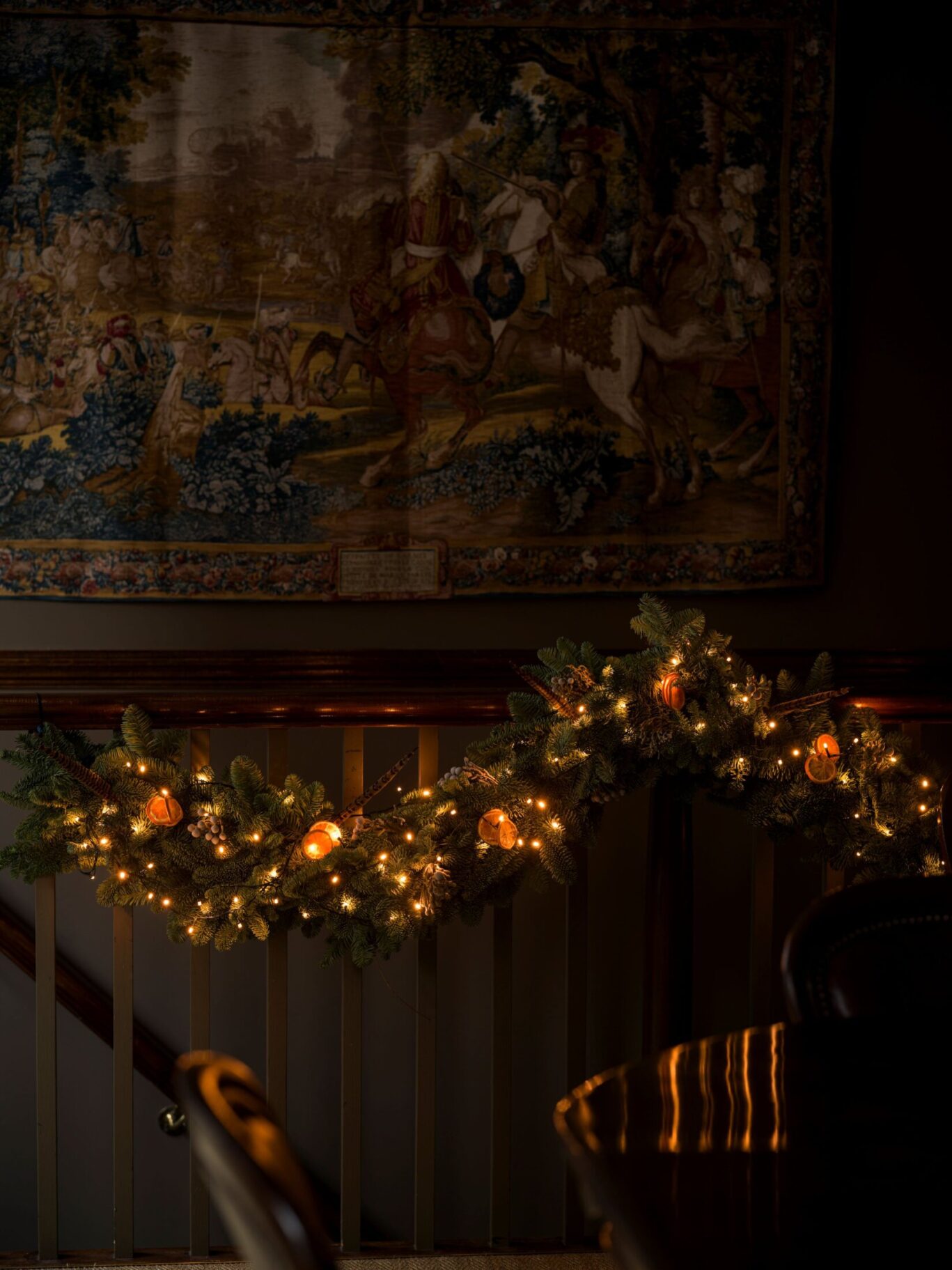 Festive garland with warm lights and dried oranges draped along a staircase railing beneath an antique tapestry at The Rookery in Clerkenwell.